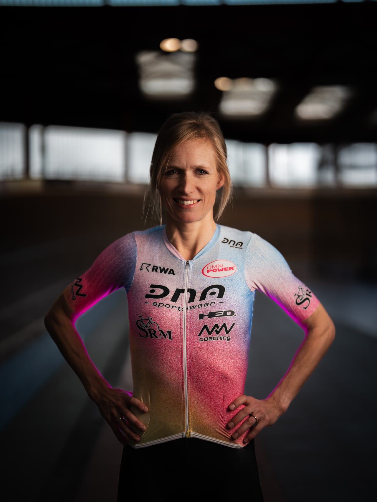 Porträt einer Radsportlerin im Teamtrikot, im Hintergrund eine Radrennbahn