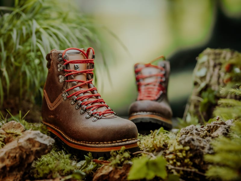 Produktfoto von braunen Wanderschuhen mit roten Schnürsenkeln auf Moos und Stein