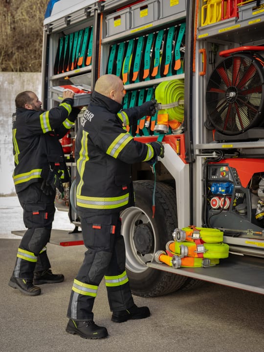 Zwei Feuerwehrleute entnehmen Ausrüstung aus einem Einsatzfahrzeug